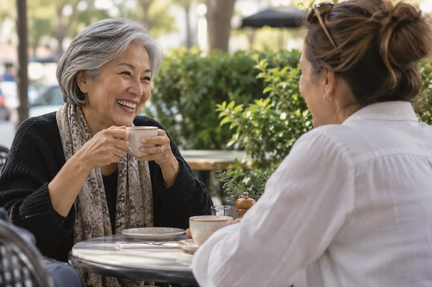Two women laughing together over coffee at an outdoor café